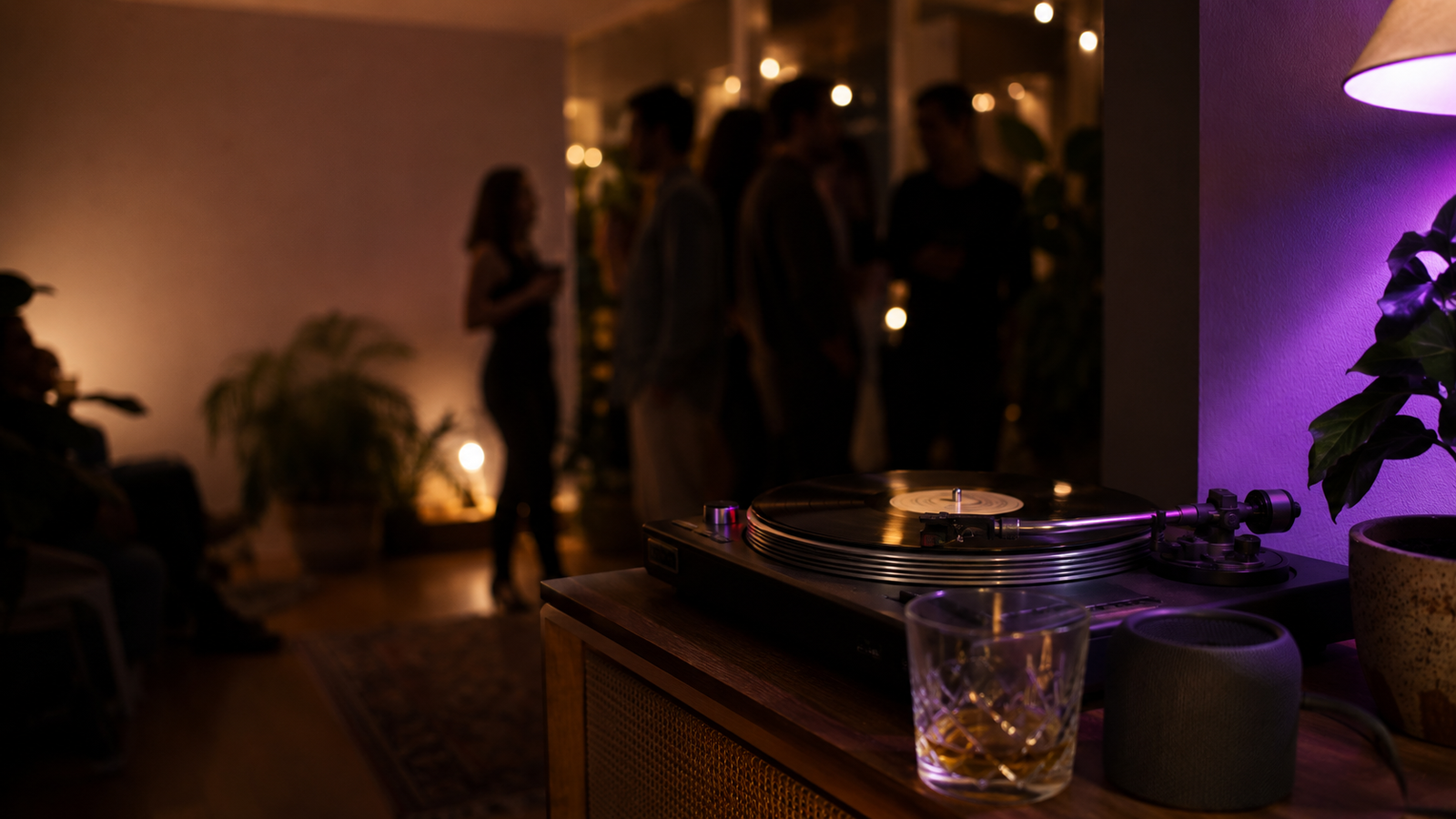 A vinyl record player on a sideboard at a warm, dimly lit house party, with guests mingling under string lights in the background and a hint of purple light to the side.